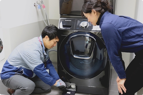 삼성전자서비스 수리 엔지니어가 출장 점검 서비스를 신청한 고객에게 플러스 원 케어 서비스의 일환으로 드럼세탁기 배수펌프 잔수 제거 방법을 설명하고 있다.